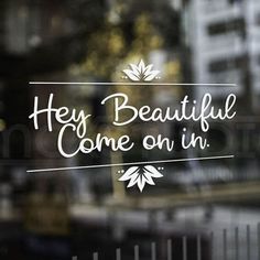 the words hey, beautiful come on in etched into a glass window with buildings behind it