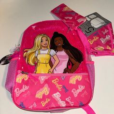 two barbie dolls are in the back pocket of a pink backpack and one is holding a camera