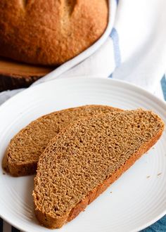 two slices of bread on a white plate next to a loaf of bread and a blue towel