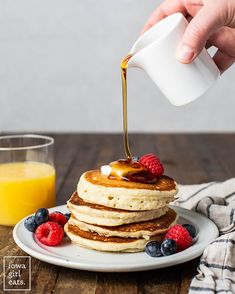 a stack of pancakes with syrup being drizzled over them and topped with berries