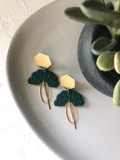 two green leaf shaped earrings sitting on top of a white plate next to a potted plant