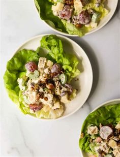 three white plates filled with lettuce and chicken salad on top of a marble counter