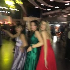 three women in long dresses standing next to each other on a dance floor at a party