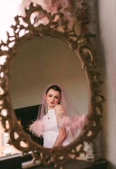 a woman is standing in front of a mirror wearing a wedding dress and pink feathers