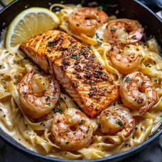 salmon and shrimp pasta in a skillet with lemon wedge garnish on the side