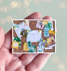 a hand holding a small cork board with pictures and magnets on it's side