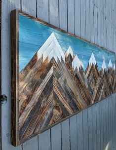 a painting hanging on the side of a building with mountains painted on it's sides