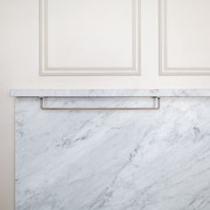 a white marble counter top with brass handles in front of a wall mounted cabinet door