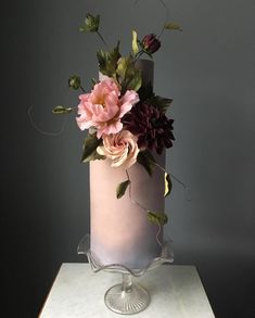 a pink and purple cake with flowers on it sitting on a white countertop next to a gray wall