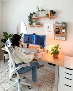 a woman sitting at a computer desk in front of a monitor and keyboard, with plants on the wall behind her