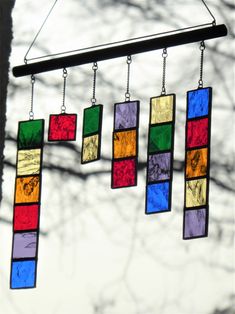 a wind chime with multicolored squares hanging from it's sides in front of a tree