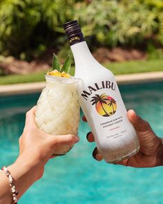 two people holding up drinks next to a swimming pool