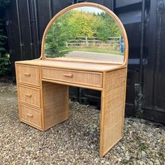 a wicker desk with a mirror on it in front of a black fence and trees