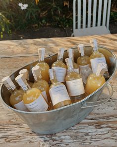 several bottles of liquid sitting in a bucket on a wooden table with white chairs behind them