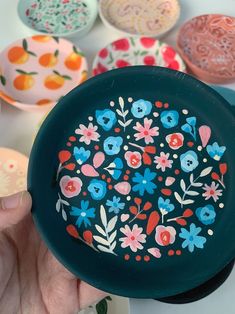 a hand holding a black plate with colorful flowers painted on it and other plates in the background