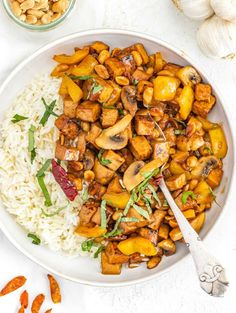 a white bowl filled with rice and vegetables next to some nuts on the side,