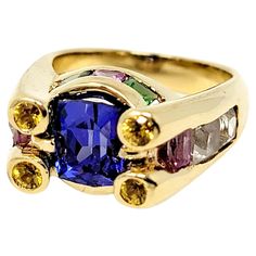 Ring size: 6 Colorful contemporary ring with unique artful design. Bursting with bold colors and sleek lines, this high profile ring will stand out on the finger and make an extraordinary statement. Ring size: 6 Metal: 18K Yellow Gold Weight: 14.40 grams Length: 10.46 mm Height: 11 mm Natural Tanzanite: 1.73 ctw Tanzanite cut: Rectangular Cushion Other stones: Tsavorite, lab-created white spinel and natural pink and yellow sapphires Stamped: 18K Estate Condition: Very good, professionally cleane Modern Gold Multi-stone Sapphire Ring, Modern Gold Sapphire Ring With Multi-stone, Modern Multi-stone Sapphire Anniversary Ring, Luxury Multicolor Rings With Center Stone, Modern Multi-stone Rings, Cocktail Ring Designs, Aquamarine Cocktail Ring, Eternity Ring Gold, Rectangular Cushion