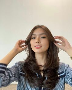 a woman with long brown hair holding her hands to her head