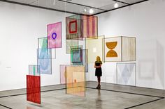 a woman standing in an art gallery looking at artwork on the walls and floor,