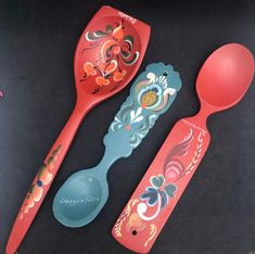 two spoons and one ladle are decorated with designs on red plastic plates,