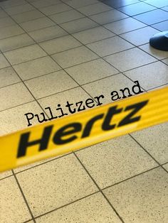 there is a yellow and black sign on the floor that says pullitzer and hertz