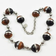 This is part of Chairish’s Costume Jewelry assortment.  Elegant modernist Balenciaga Paris signed necklace. It features a choker shape with a chromed metal chain ornate with geometric half-sphere cabochons in exotic woods. Signed with chrome metal tag at clasp: "BB - Balenciaga - Made in France". Spring-ring closing clasp with adjustable chain for length flexibility.  Measurements: necklace's total length is 19.69 in long (50 cm) - each cabochon element is 0.82 in diameter (2 cm).  Please see th Modernist Metal Necklace With Polished Finish, Modern Silver Sphere Necklace, Modern Round Cabochon Necklace, Modern Brown Round Jewelry, Elegant Necklaces With Wooden Beads, Elegant Wooden Beads Necklace, Modern Cabochon Necklace, Elegant Brown Necklace With Polished Finish, Unique Silver Jewelry With Wooden Beads