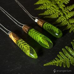 three necklaces with green leaves on them sitting next to a fern leaf and silver chain