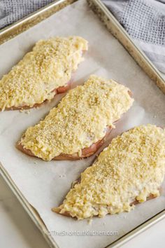 three pieces of bread with cheese on top in a metal baking pan next to a blue and white towel