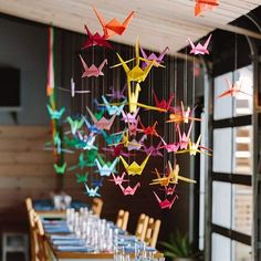 colorful origami cranes hang from the ceiling above a long table with wine glasses on it