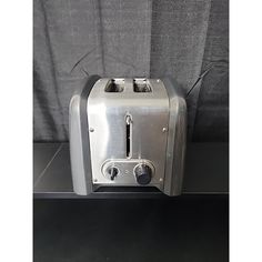 a silver toaster sitting on top of a counter next to a gray cloth covered wall