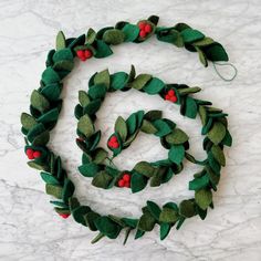 a wreath made out of felt with red berries and green leaves on the top, sitting on a marble surface