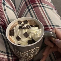 a person sitting on a couch holding a cup of ice cream with chocolate chunks in it