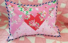 a pink pillow with a red heart in the center on a quilted bedspread