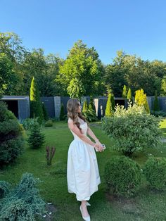 a woman in a white dress walking through a garden