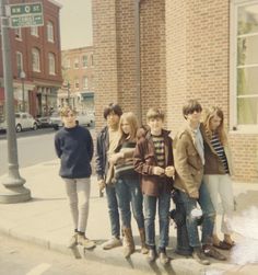 a group of young people standing next to each other on the side of a street