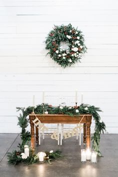 a table decorated with greenery and candles for an outdoor wedding ceremony in front of a white wall