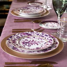 the table is set with purple and gold plates, silverware, and wine glasses