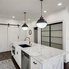 a kitchen with white cabinets and marble counter tops, two pendant lights over the sink