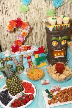 an image of a birthday party with food on the table and in front of it is a tiki mask