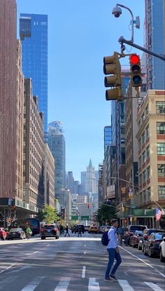 a man is crossing the street in front of some tall buildings and traffic lights on a sunny day