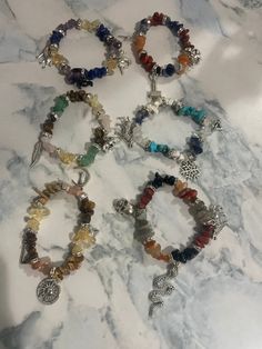 "Inspired by the Norse Deities, these beaded bracelets feature genuine chip gemstone beads that are paired with crystal rondel spacer beads and accented with charms. Odin: Features a mix of Lapis, Citrine, and Amethyst beads. It is accented with a black raven, a wolf, and a horse charm. Freyja: Features a mix of Aventurine, Citrine, Rose Quartz, and Tiger Eye. It is accented with a cat in the moon, a pig, and a feather charm. Thor: Features a mix of Carnelian, Sodalite, and Red Jasper beads. It is accented with a hammer, a goat, and a lightning bolt charm. Skadi: Features a mix of Turquoise, Howlite, Clear Quartz, and Sodalite beads. It is accented with a snowflake, a bow, and a wolf charm. Angrboda: Features a mix of Obsidian, Red Jasper, Labradorite, and Carnelian chip beads. It is accen Crystal Bracelets Aesthetic, Norse Deities, Chip Bead Jewelry, Year Aesthetic, Bracelets Bead, Black Raven, Viking Bracelet, Hand Necklace, Feather Charms