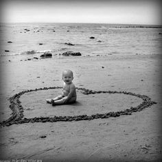 a baby sitting in the sand with a heart drawn on it