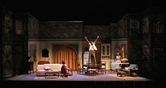 two people standing on top of a stage in front of a couch and table with chairs