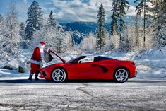 a santa clause standing next to a red sports car