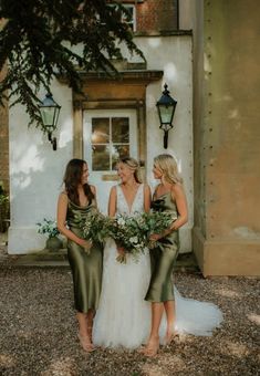 three bridesmaids standing in front of a white house with greenery and flowers