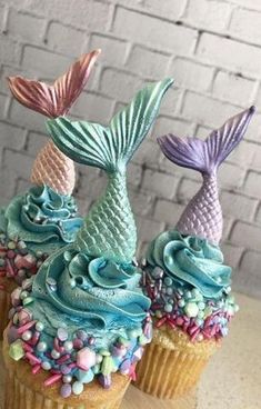 three cupcakes with blue frosting and mermaid tail decorations on top of them