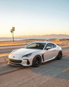 a white sports car parked on the side of the road next to the ocean and palm trees