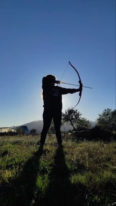 a woman standing in the grass with a bow and arrow