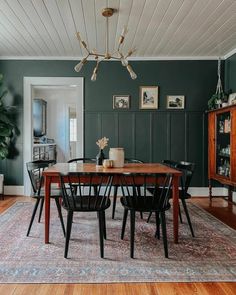 a dining room with green walls and wooden flooring is pictured in this image, there are several chairs around the table