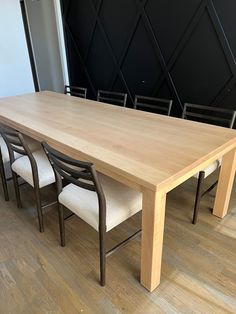 a wooden table with chairs around it on a hard wood flooring area next to a black wall